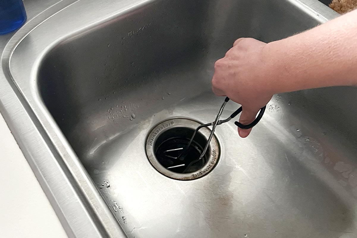 A person unclogging a kitchen sink with tongs.