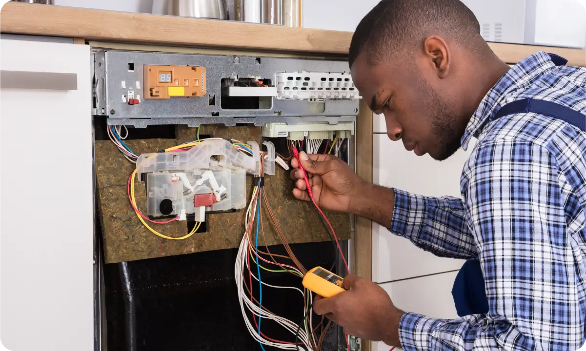 A male in a blue plaid shirt rewiring a dishwasher.