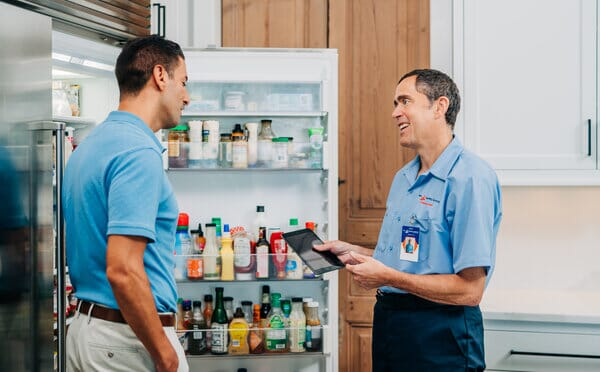 Mr.Appliance tech and homeowner standing in kitchen in front of refrigerator.